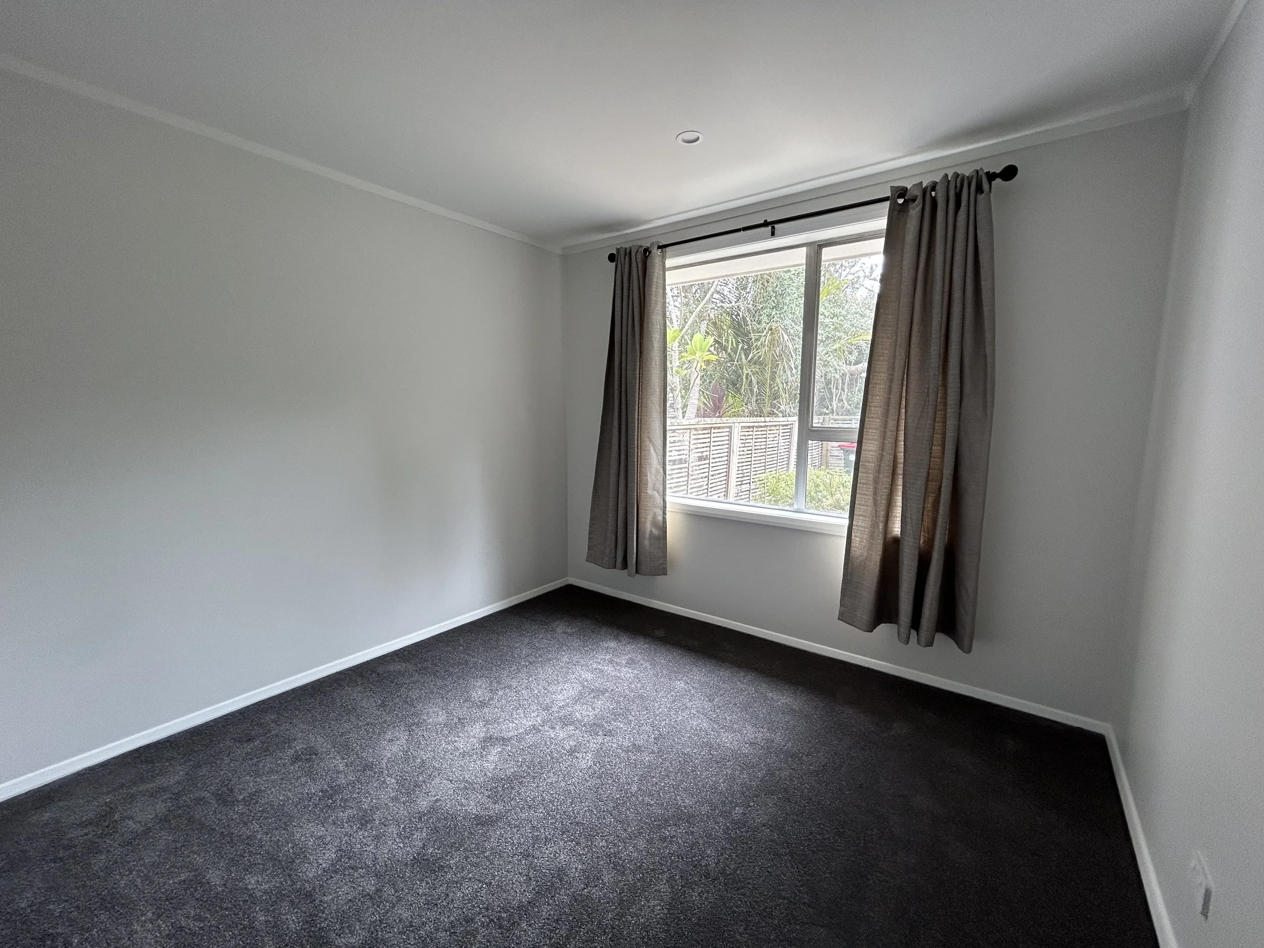 Empty bedroom with grey carpet, white walls, and a window with grey curtains